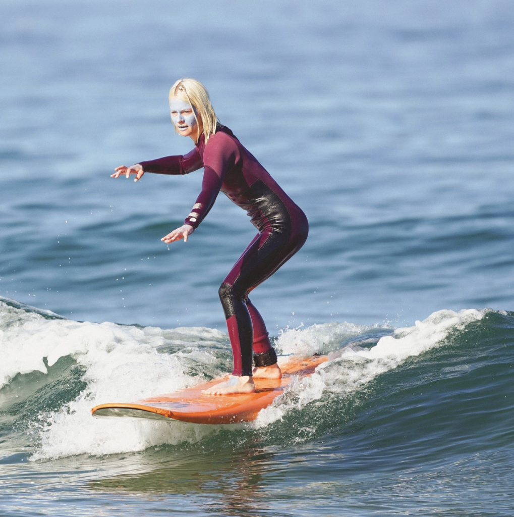 Junge Frau beim Surfen mit blauer Sonnencreme im Gesicht