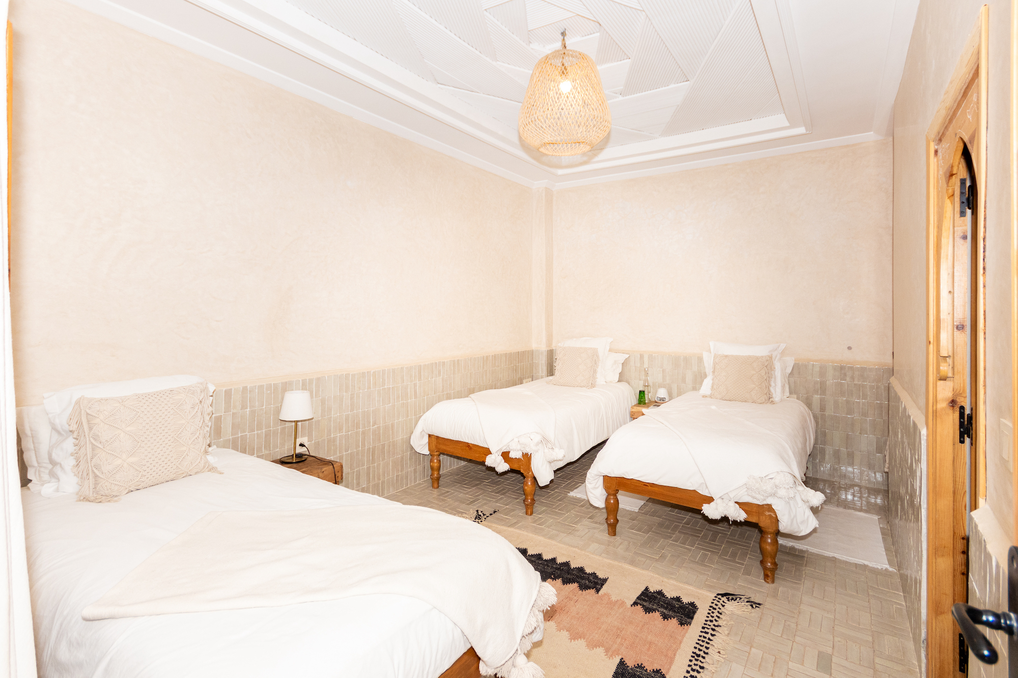 A room in a maroccain riad with light painted walls and 3 beds with white bed sheets